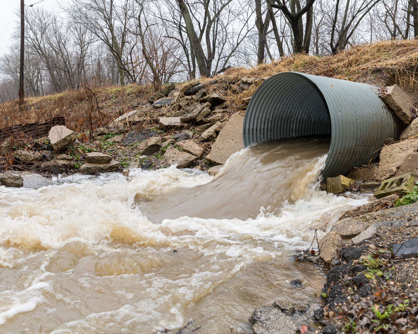 Closeup motion blur of storm water runoff flowing through metal drainage culver under road. Storms brought heavy rain and flash flooding
