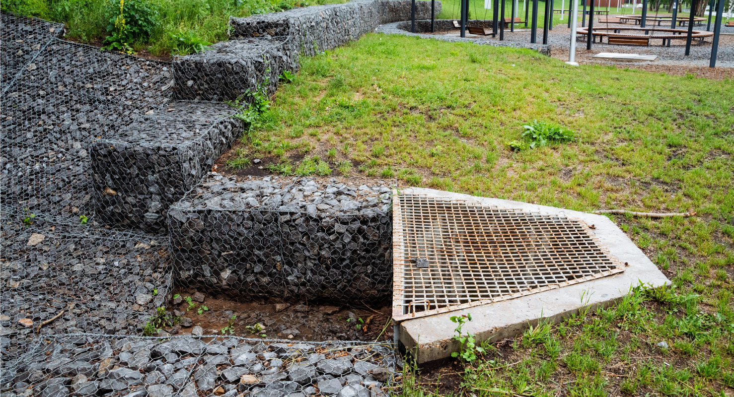 An outdoor gravel and metal grate drainage system is implemented in an urban park featuring walking paths, promoting sustainability and efficient stormwater management