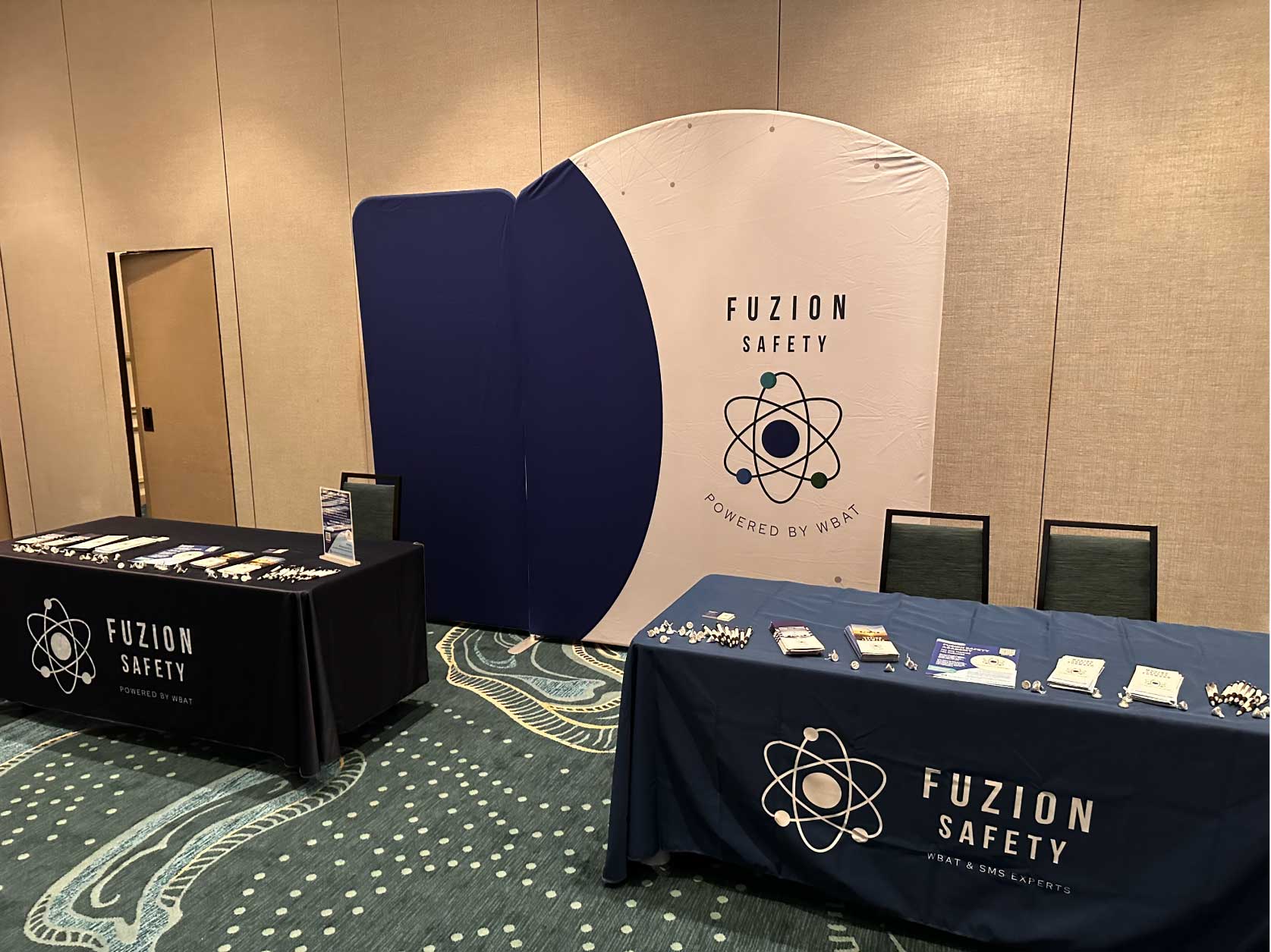 Fuzion Safety booth setup in a room for safety conference. Booth includes two tables and a backdrop banner behind tables.