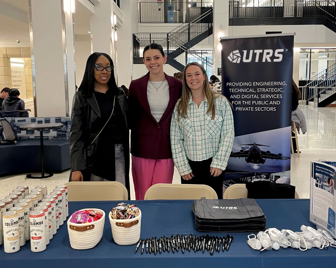 Pictured are three UTRS HR employees standing at the UTRS branded booth in the Jones Family Learning Commons at Villanova University