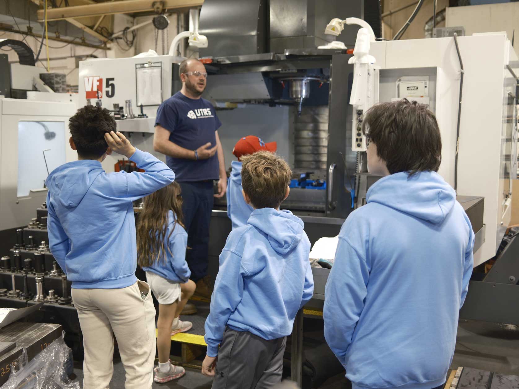 Children learning from a UTRS Advanced Manufacturing machinist how the Haas VF5 CNC machine operates.