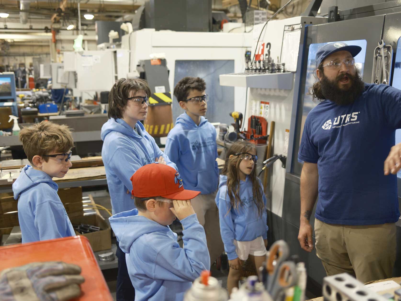 A UTRS Advanced Manufacturing Robbinsville machinist showing children how the CNC machine controls will make their personalized aluminum cubes.