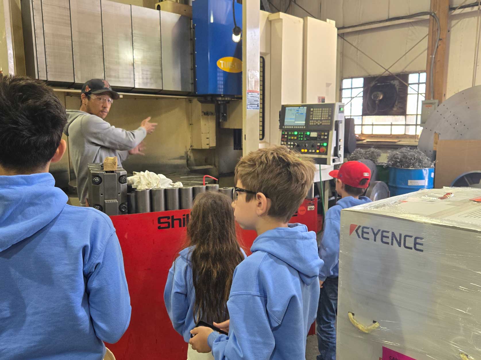 Children learning from a UTRS Advanced Manufacturing machinist how the Shibaura Vertical Turning Center CNC machine operates.