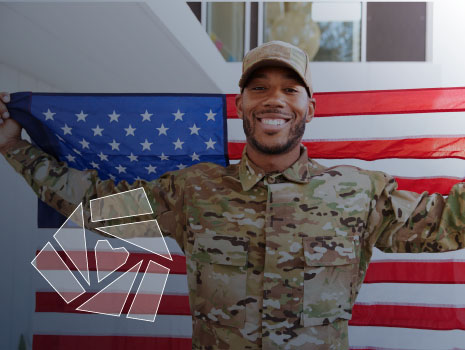 Close up of African American soldier standing outside modern building holding US flag, smiling to camera.