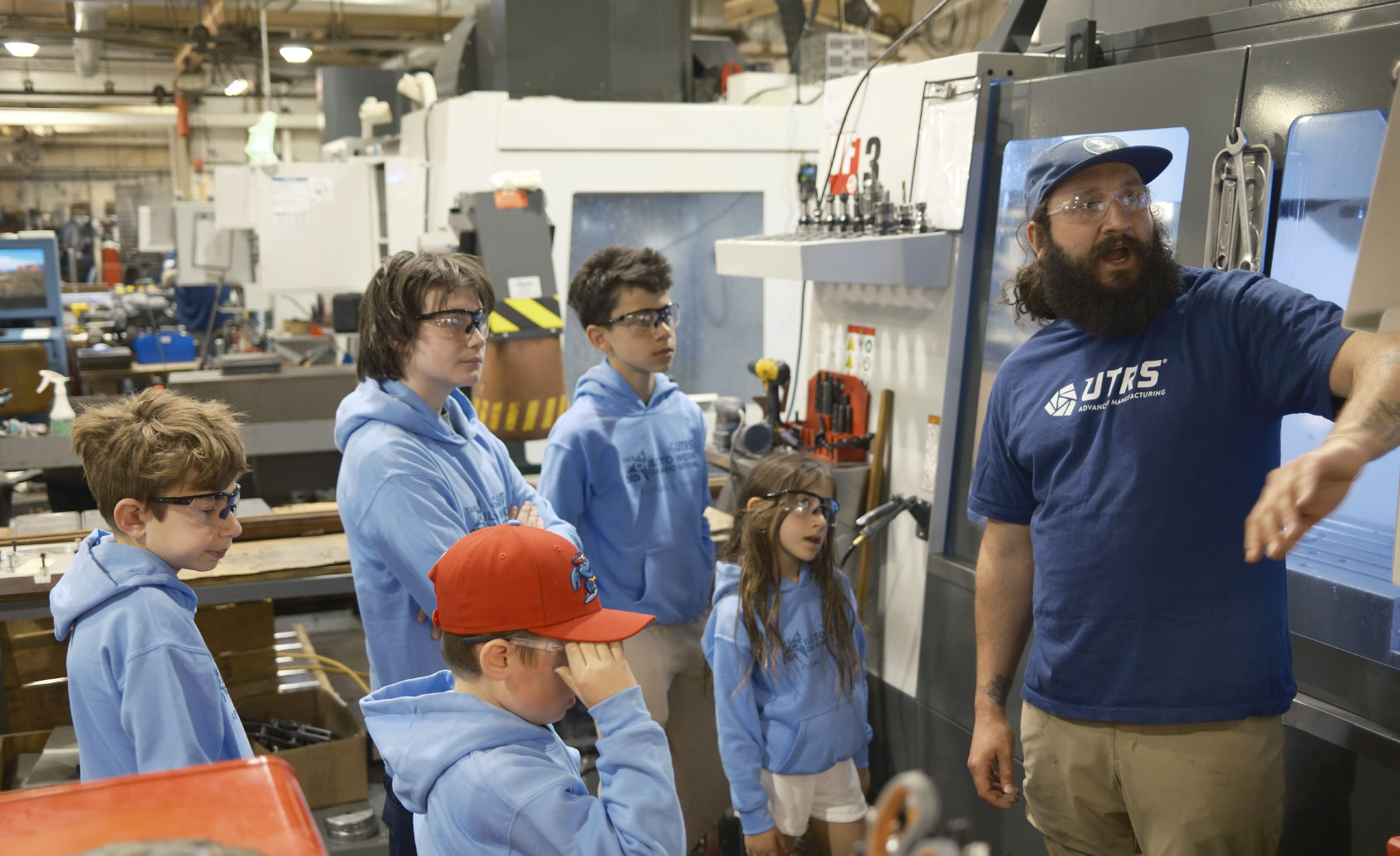 A UTRS Advanced Manufacturing Robbinsville machinist showing children how the CNC machine controls will make their personalized aluminum cubes.