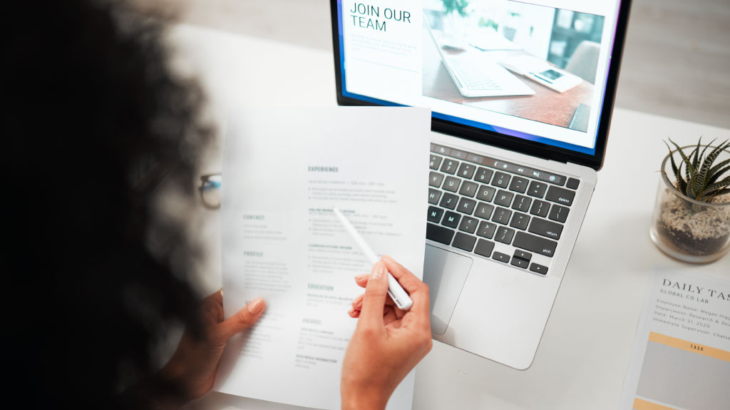 Hands, pen and human resources with CV, laptop with hiring news on company website and recruitment in office. Person reading resume, employee choice and onboarding, job application and information